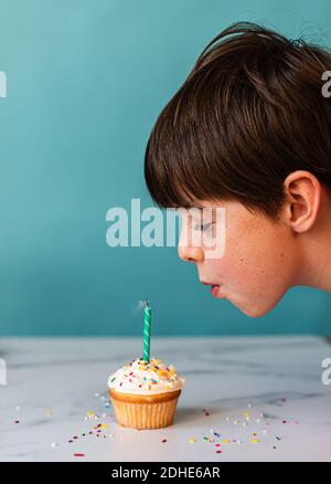 Young boy blowing out a candle on cupcake with frosting and sprinkles. Stock Photo