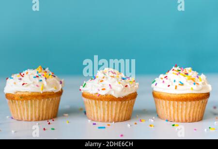 Cupcakes with sprinkles on white table with blue background. Stock Photo