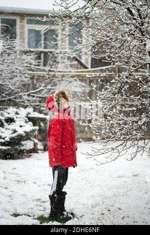 Boy in red winter jacket standing outside in a yard on a snowy day. Stock Photo