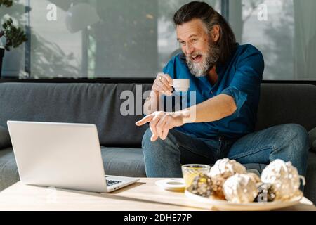 Mature man with beard talking on the phone and drinking coffee sitting Stock Photo
