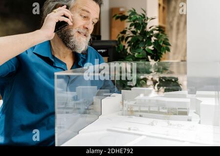 Mature man with a beard talking on the phone and looking at a model of Stock Photo