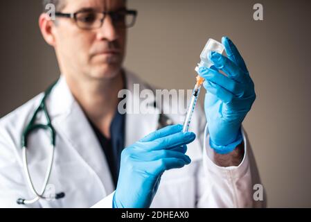 Doctor in white coat drawing vaccine into a syringe for injection. Stock Photo