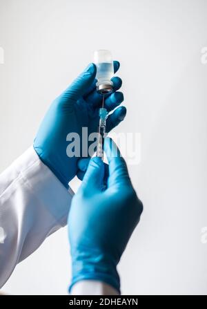 Hands in gloves drawing vaccine into syringe on white background. Stock Photo