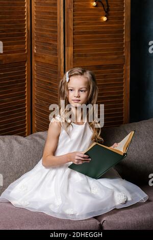 Happy child opening Christmas book. Xmas holiday concept. Girl read a book in decorated living room with Christmas tree