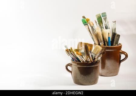 Artistic brushes and painting tools in old clay/ceramic pots on white neutral background. Stock Photo