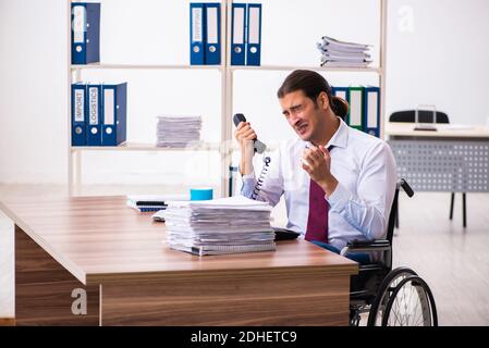 Young male employee after accident in wheel-chair at workplace Stock Photo