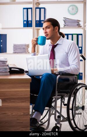 Young male employee after accident in wheel-chair at workplace Stock Photo