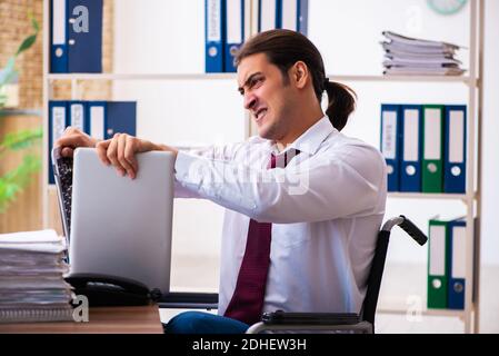 Young male employee after accident in wheel-chair at workplace Stock Photo