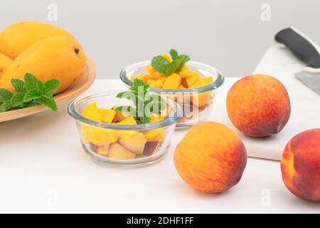 Fruit salad in a glass bowls. Sliced mango, peaches mint leaf close up on a kitchen table. Stock Photo