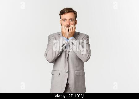 Portrait of handsome businessman in grey suit, looking startled and gasping, standing scared over white background Stock Photo