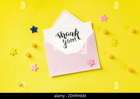 Hand written Thank You card in a pink envelope, overhead shot on a yellow background Stock Photo
