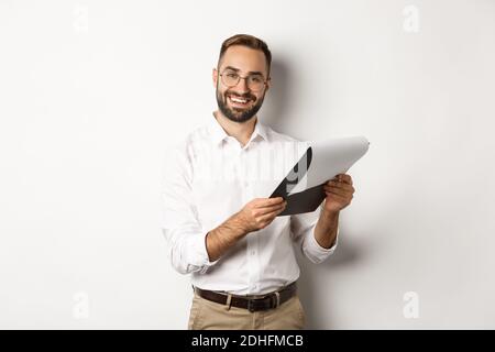 Employer looking satisfied at CV, reading document and smiling, standing over white background Stock Photo