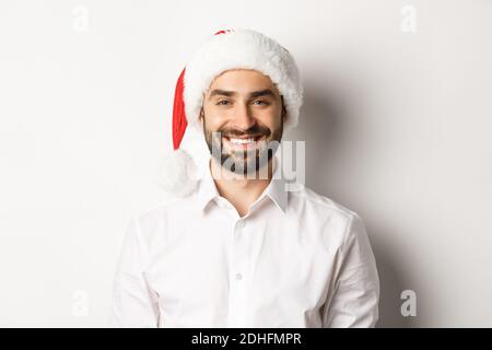 Close-up of happy bearded man celebrating christmas, wearing santa party hat and smiling, standing over white background Stock Photo