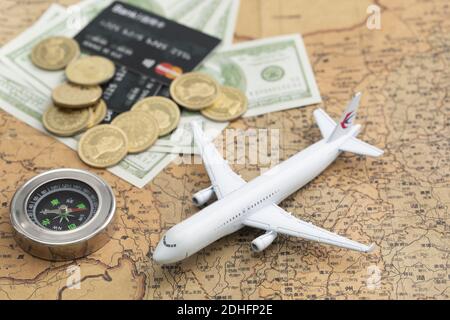 A selective focus closeup of a toy airplane, coins, ATM, compass, and dollar paper bills on a world map background-concept travel Stock Photo