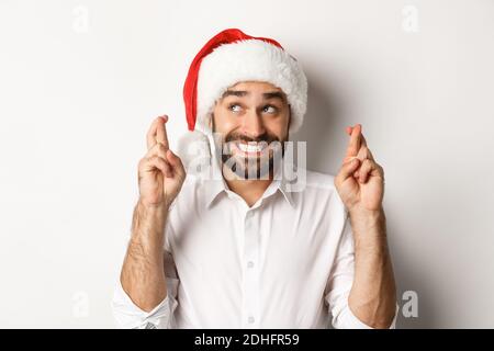 Party, winter holidays and celebration concept. Happy man in santa hat making christmas wish, cross fingers for good luck and sm Stock Photo