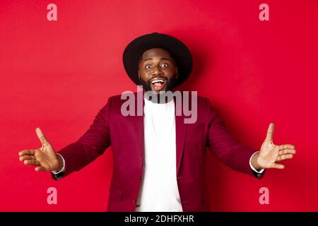 Fashion and party concept. Pleased handsome Black man spread hands in welcome gesture, reaching to receive something, looking am Stock Photo
