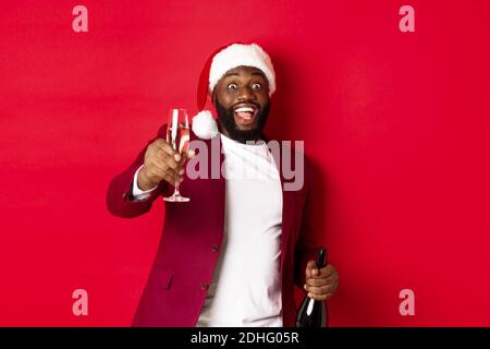 Christmas, party and holidays concept. Handsome Black man in santa hat raising glass of champagne and smiling, saying toast, cel Stock Photo