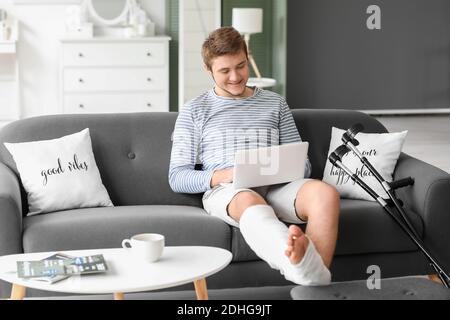Young man with broken leg using laptop at home Stock Photo