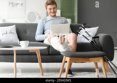 Young man with broken leg using laptop at home Stock Photo