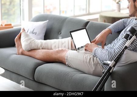 Young man with broken leg using laptop at home Stock Photo