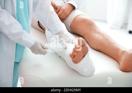 Doctor putting broken leg of young man in plaster Stock Photo