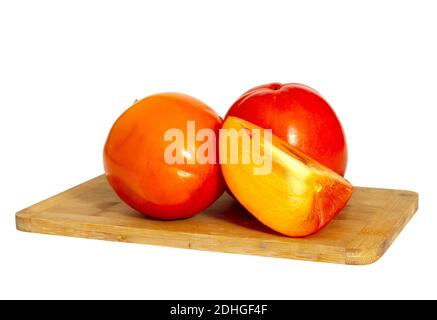 A closeup of persimmon fruit on a wooden chopping board on a white background Stock Photo
