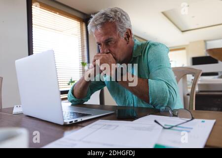 Worried senior caucasian man sitting at table using laptop paying bills Stock Photo