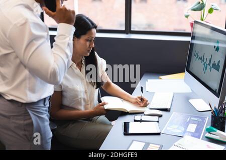 Mixed race businesswoman and businessman using smartphone and computer in office Stock Photo