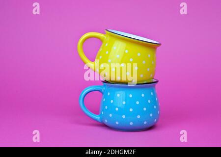 A closeup of yellow and blue mugs with polka dots on top of each other isolated on a pink background Stock Photo