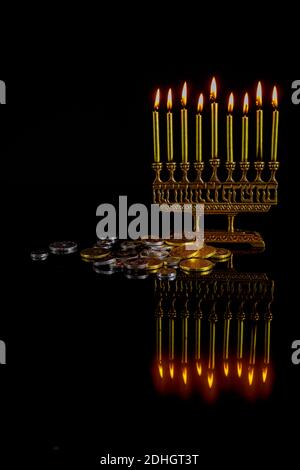 Menorah with golden burning candles, chocolate coins and reflection on surface for Hanukkah jewish holiday. Stock Photo