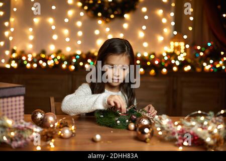 happy cute little child girl makes a handmade Christmas wreath at home. Stock Photo