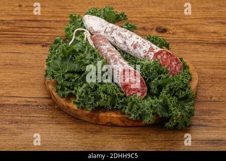 Spanish Fuet sausage with salad leaves over wooden background Stock Photo