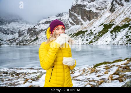 A cold woman tourist is drinking hot tea in a beautiful mountain landscape. Stock Photo