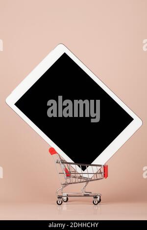 tablet pc on red mini shop cart trolley on beige background, buying at home and online shopping concept, close up copy space  Stock Photo