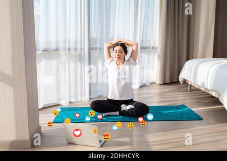 Young pretty woman in sportswear doing yoga live online. Emoticons and emojis fly around the laptop. Top view. The concept of social networks and blog Stock Photo