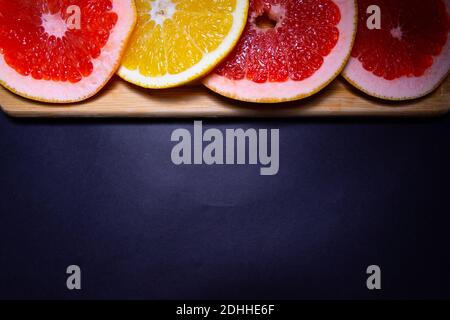 Oranges and red fruit on black wooden boards. Halves of juicy orange on black background. Orange fruit, citrus minimal concept. Top view, copy space
