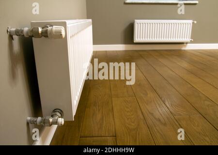 White metal heating radiator mounted on gray wall inside a room. Stock Photo