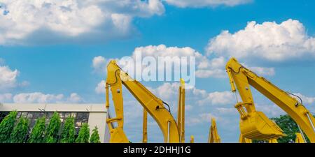 Yellow backhoe with hydraulic piston arm against blue sky. Huge bulldozer parked at parking lot near sale office. Bulldozer dealership. Hydraulic. Stock Photo