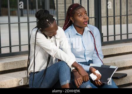 group of young students working together, are sitting on stairs outside with document and a smart phone in casual outfit. Stock Photo