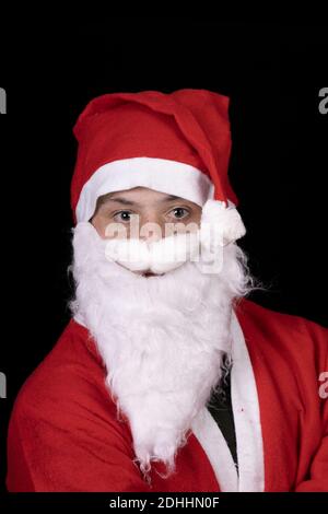 A young male with down syndrome posing in a Santa Claus costume isolated on a black background Stock Photo