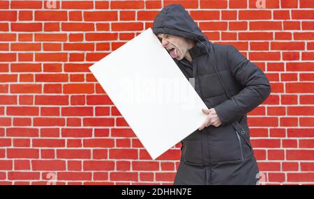 A closeup of a male trying to lick the white canvas for painting on red-bricked wall background Stock Photo