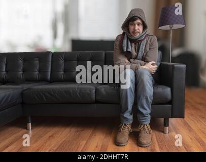 Young man sitting on couch is feeling cold at home. Stock Photo