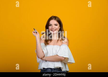 Woman with pen. Cheerful young female in formalwear holding pen and smiling while standing isolated on yellow Stock Photo
