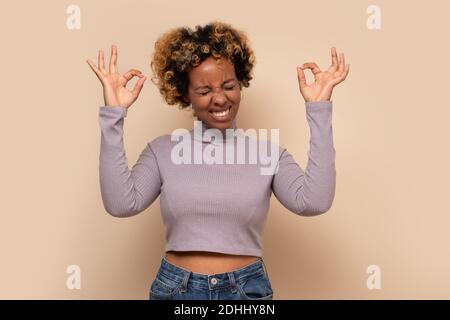 African young woman trying to meditate, standing with lifted hands and yoga gesture. Studio shot Stock Photo
