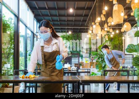 Portrait attractive Asian restaurant employee wear face mask and face shield cleaning table and floor with alcohol and wet wipe before welcome custome Stock Photo