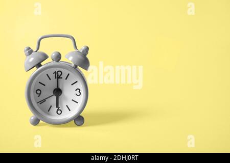 Gray analogue alarm clock showing six in the morning on background of the illuminating yellow tone. Copy space. The main color trend of the year 2021. Stock Photo