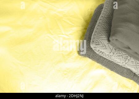 Stack of folded warm gray knitted sweaters of different tones on yellow background with copy space. Laundry concept. Main color trend of the year 2021 Stock Photo