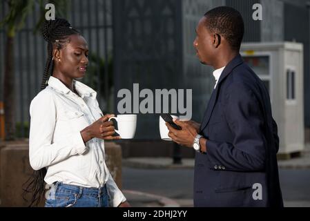 Two serious businessmen drinking coffee to take away. Man and middle-aged woman in official shirt standing outside. Coffee break concept Stock Photo