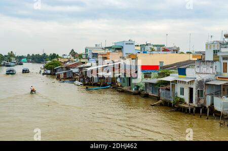 Mekong Delta in Vietnam. Boats in river with brown water. Houses of local citizens on the bank of river. Stock Photo