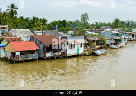 Mekong Delta in Vietnam. Boats in river with brown water. Houses of local citizens on the bank of river. Stock Photo